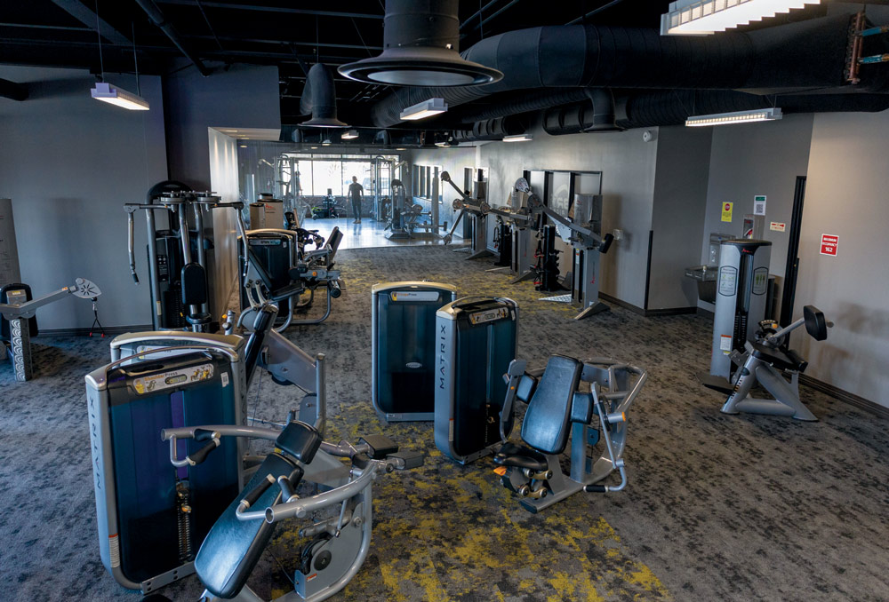 Wide view of a gym floor featuring various Matrix strength training machines and grey industrial ceilings.