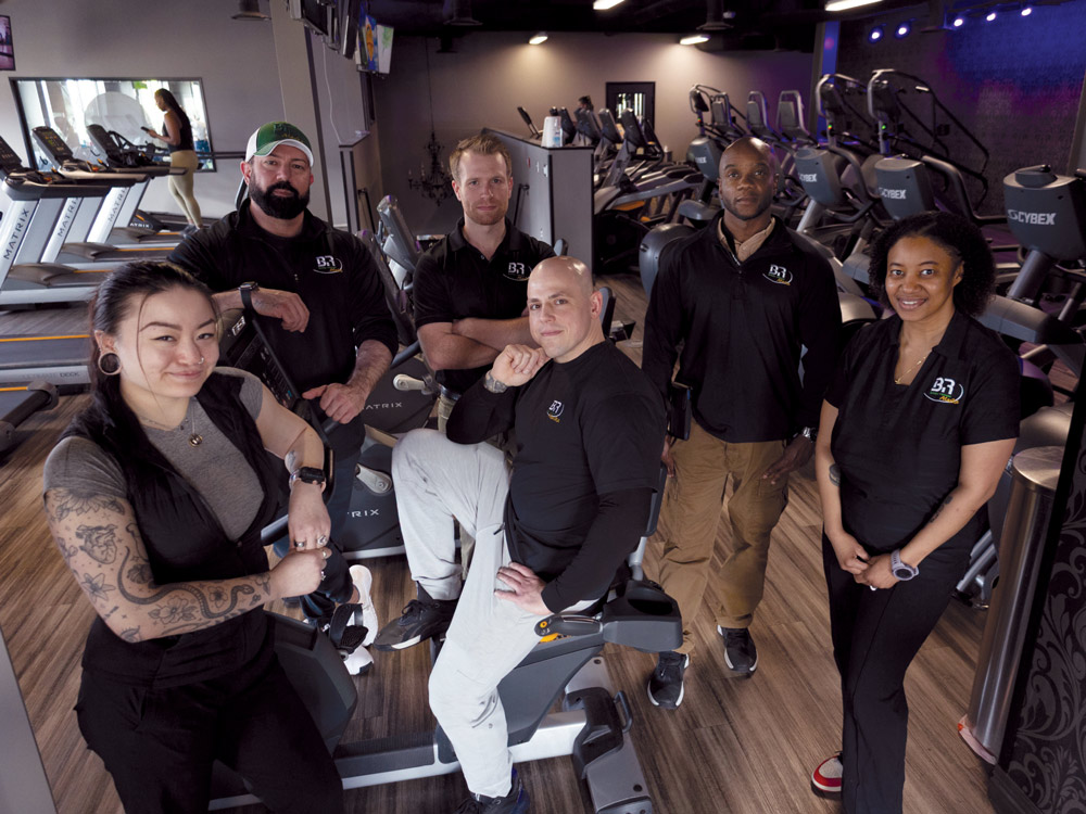 Six fitness staff members in black Body Renew branded shirts posing together on the gym floor.
