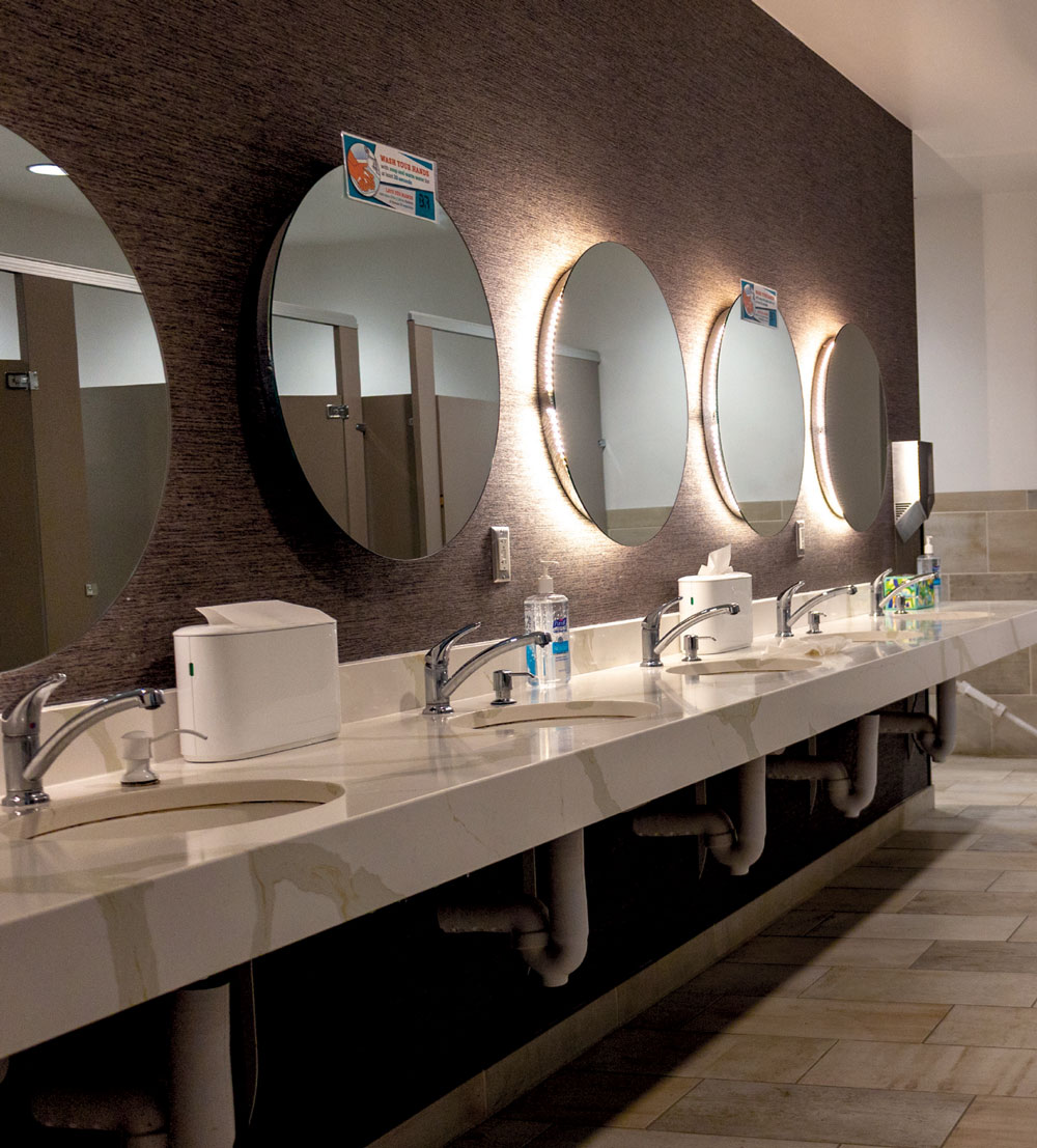 Modern gym restroom featuring a long white vanity with five circular backlit mirrors and chrome faucets.