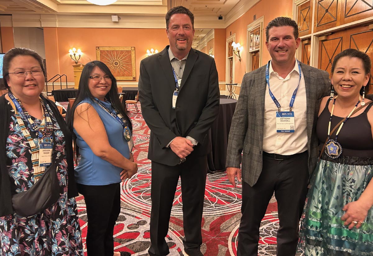 A group of five smiling conference attendees, some wearing traditional Indigenous jewelry, pose together in a large ballroom.