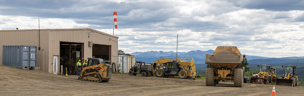 Heavy machinery, including a large dump truck and loaders, parked near a maintenance building.