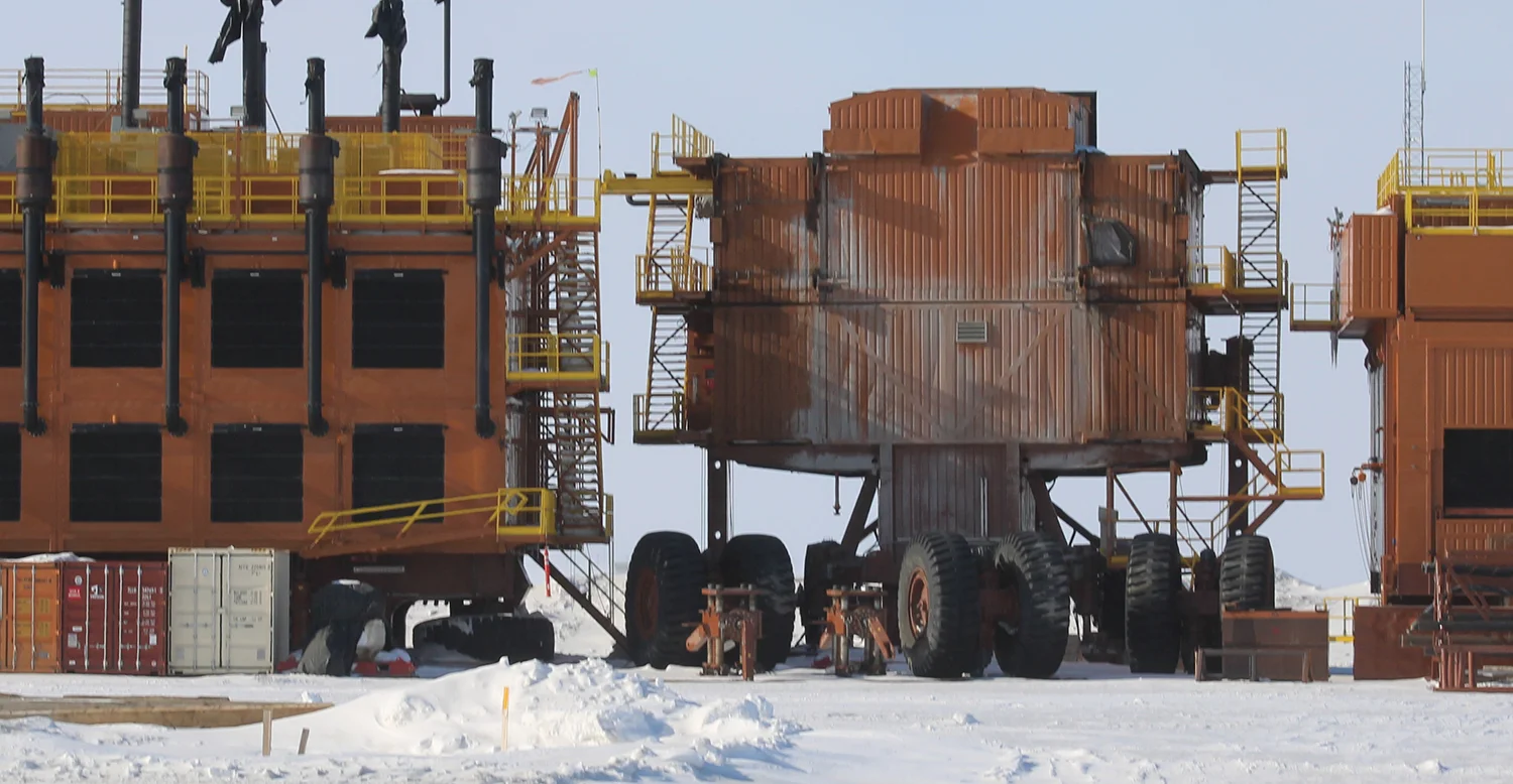 Massive orange and brown industrial modules on large, heavy-duty wheels sit parked on a flat, snow-covered landscape under an overcast sky.