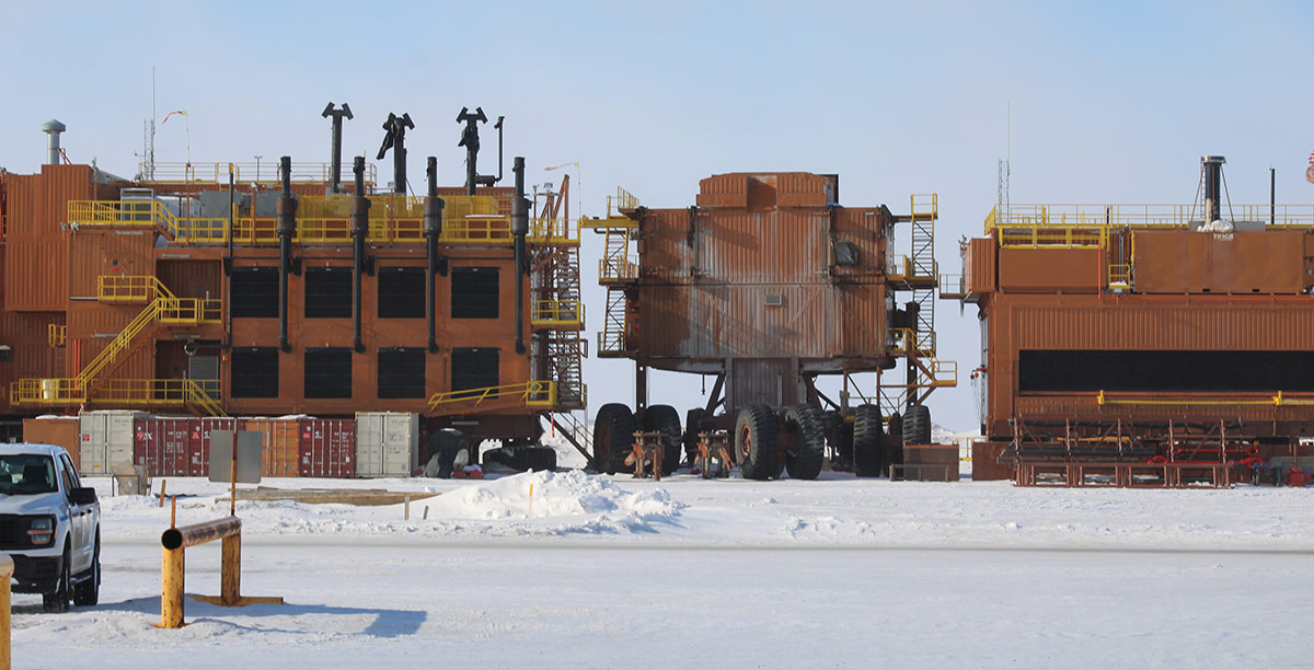 Large, multi-story industrial machinery units equipped with massive wheels sit in a snow-covered arctic landscape.