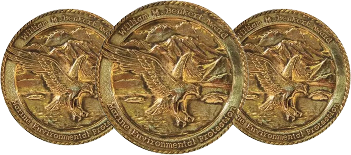 Three overlapping golden medals featuring an eagle in flight and the text "William M. Benkert Award Marine Environmental Protection."