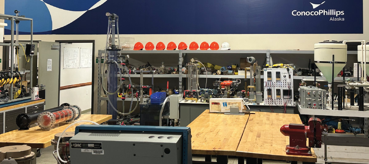 An industrial training laboratory featuring workbenches, testing equipment, and a wall displaying the ConocoPhillips Alaska logo.