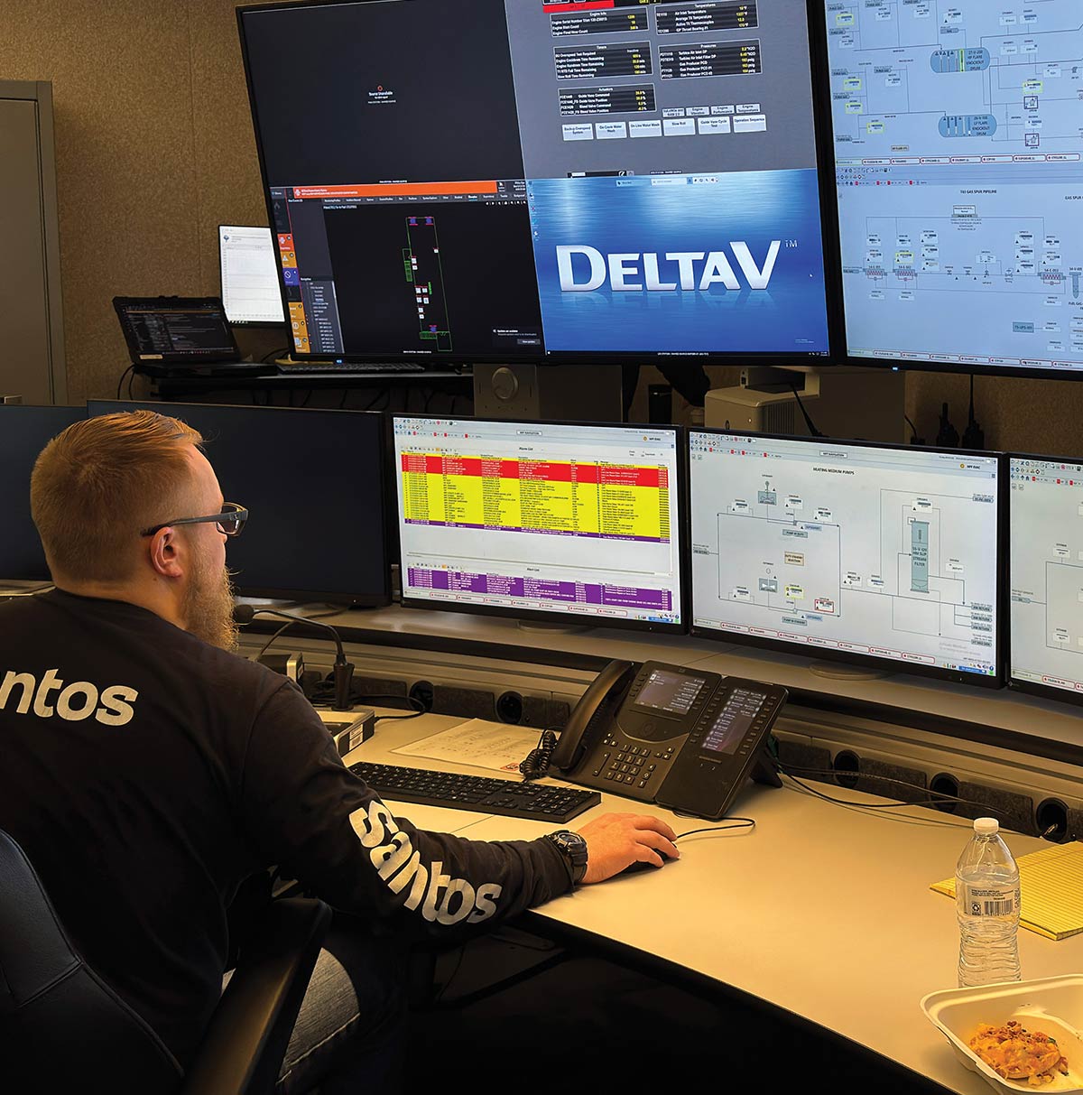An operator wearing a black Santos shirt sits at a desk in a control room, monitoring multiple computer screens displaying data, technical diagrams, and a central DeltaV logo.