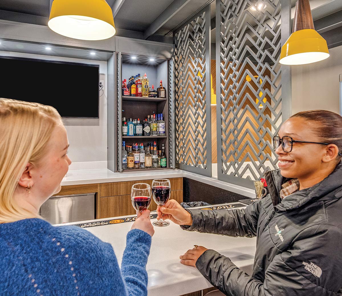 Two women smile and toast with glasses of red wine at a bar.