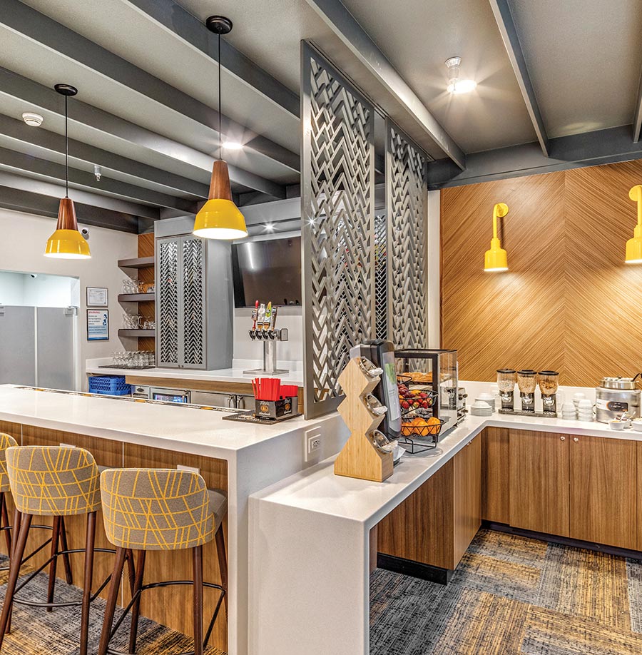 A modern hotel bar and breakfast station with wood panels and yellow lamps.