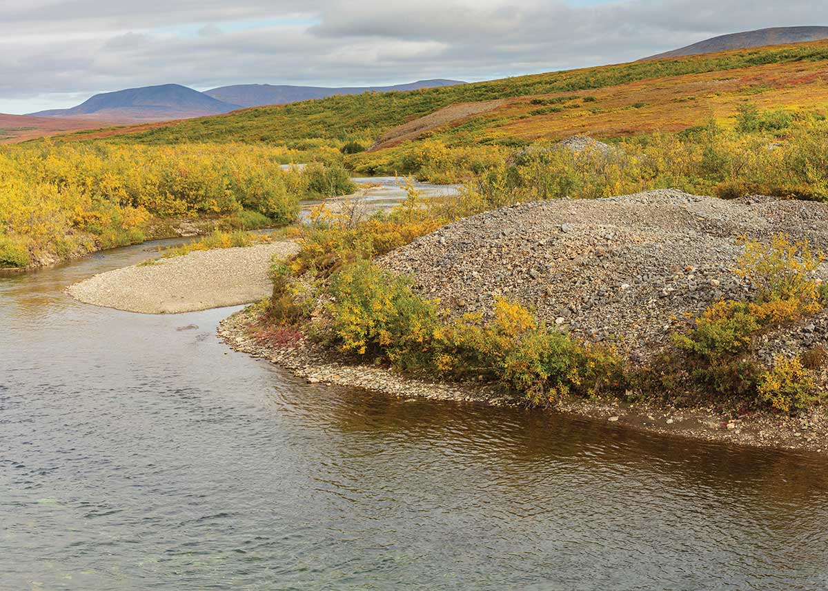 A winding river flows past gravel piles and rolling tundra hills.