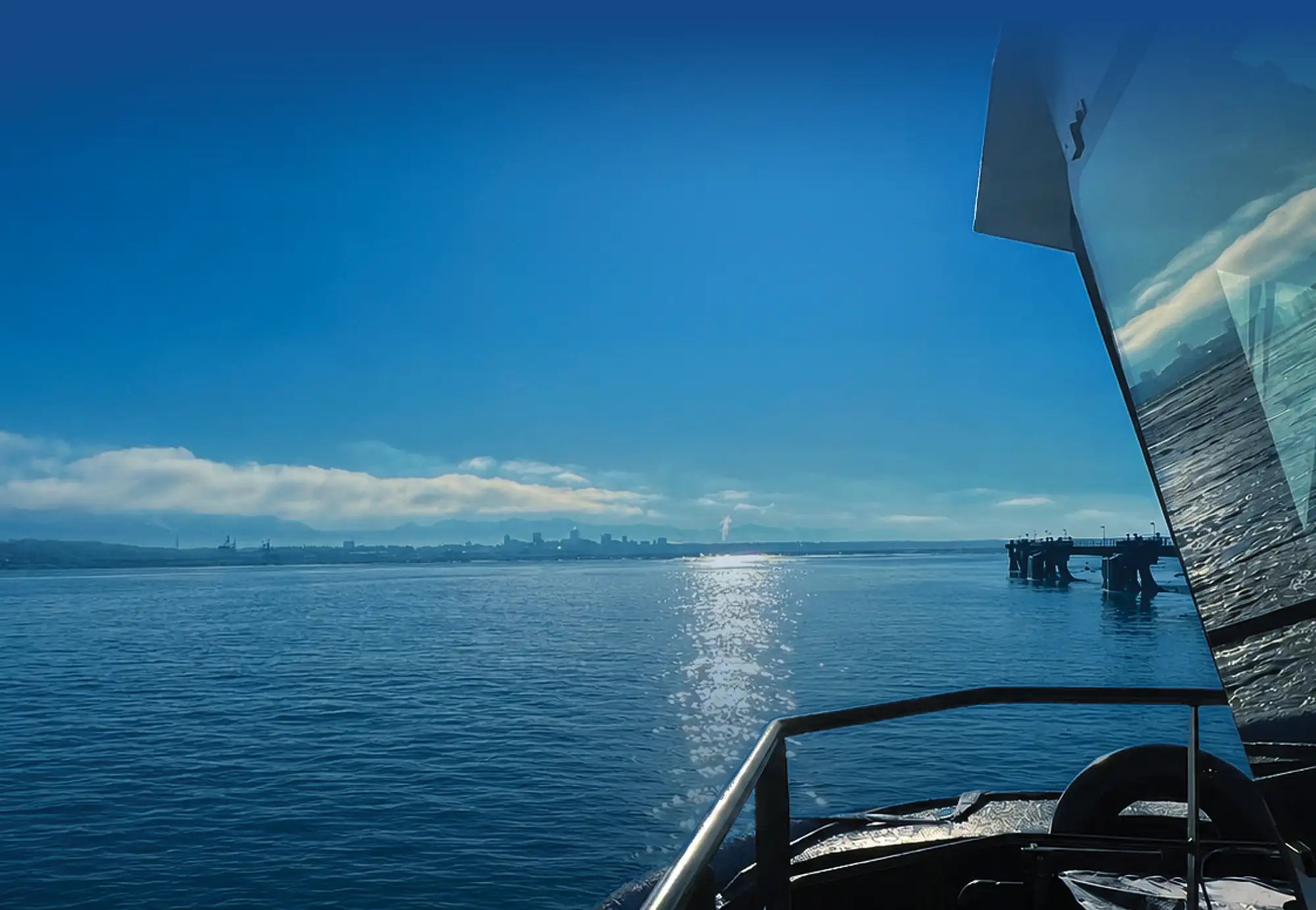 View from the deck of a boat looking across calm blue water toward a distant city skyline under a clear, bright sky.