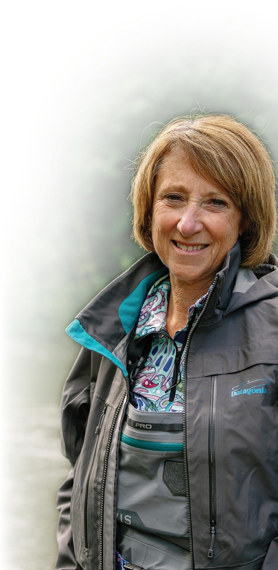 A close-up portrait of a woman wearing waders and an outdoor jacket.