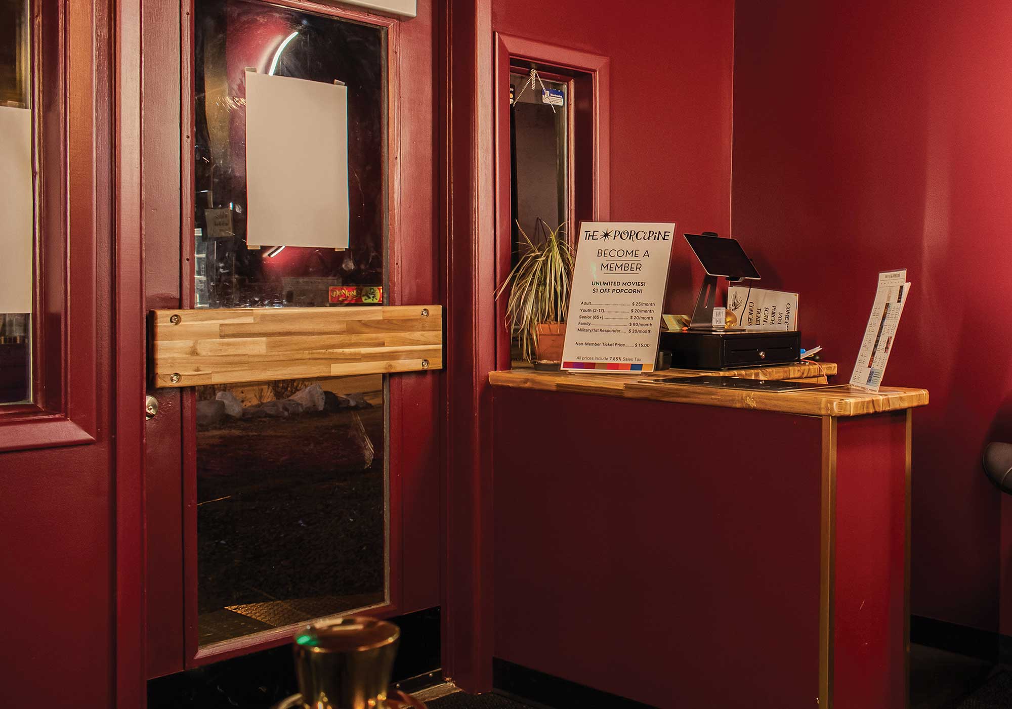 A theater counter displaying pricing signage for "The Porcupine" membership options alongside a ticket register.