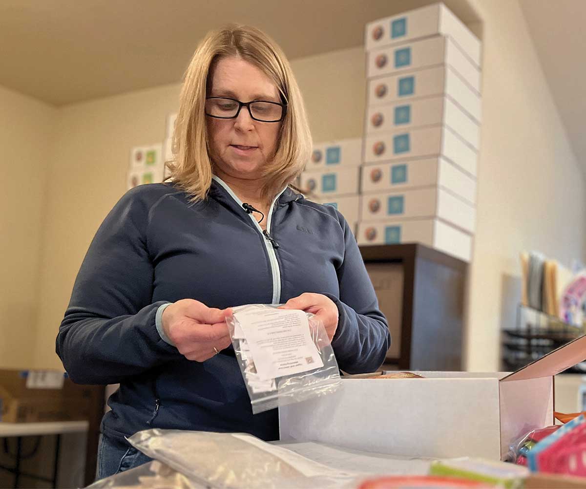 A woman assembling learning kit items near stacked supply boxes.