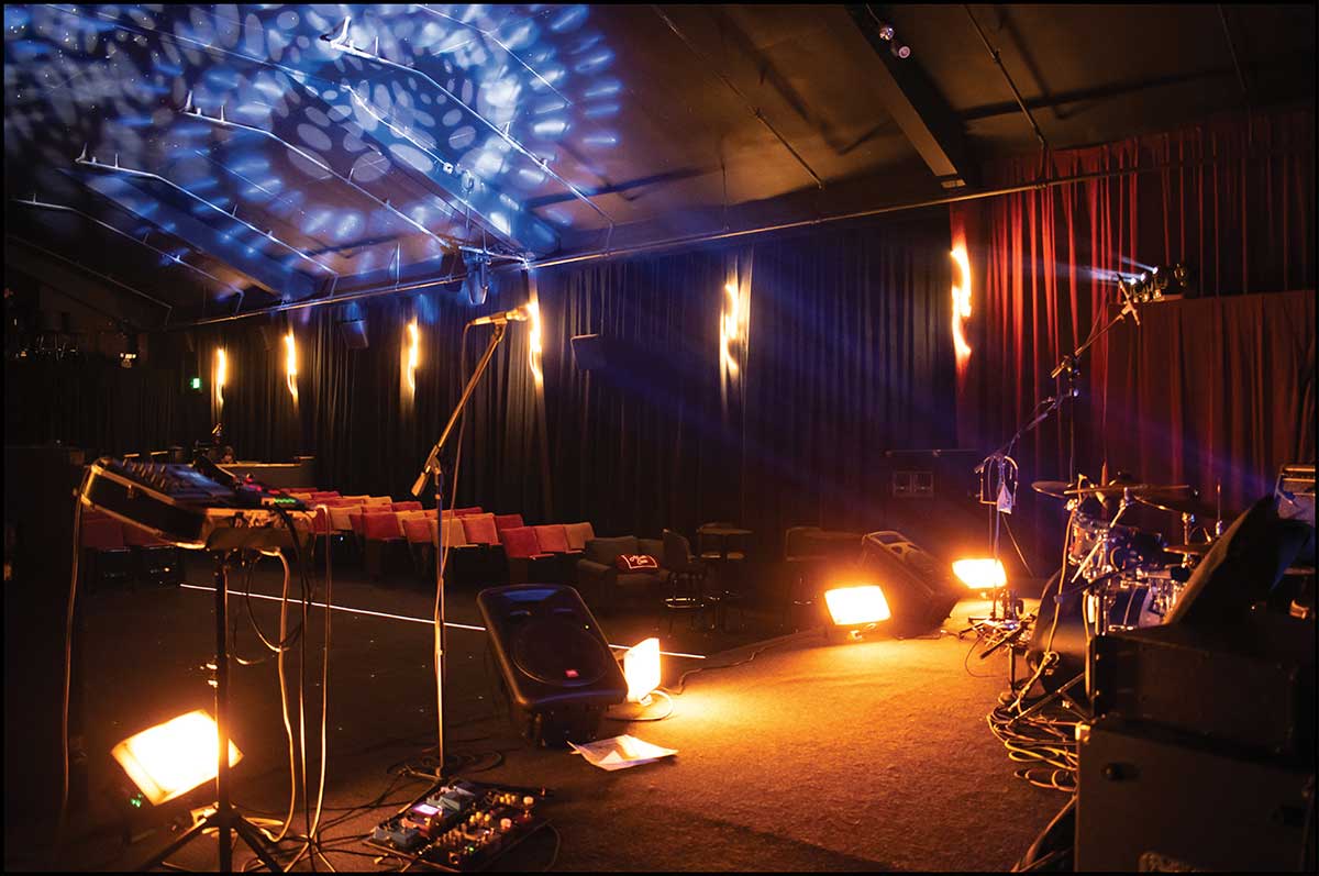 A music stage setup inside an auditorium with stage lighting and instruments.