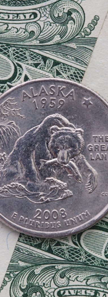 An Alaska state quarter resting on United States currency.