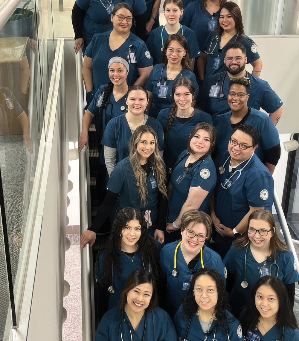 Group of nursing students wearing blue scrubs posing together on a staircase.