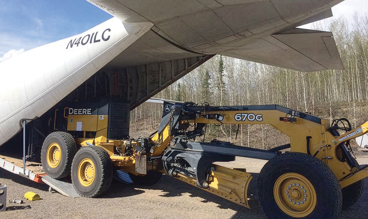 A yellow John Deere 670G motor grader being loaded into the open rear cargo bay of a large transport airplane.