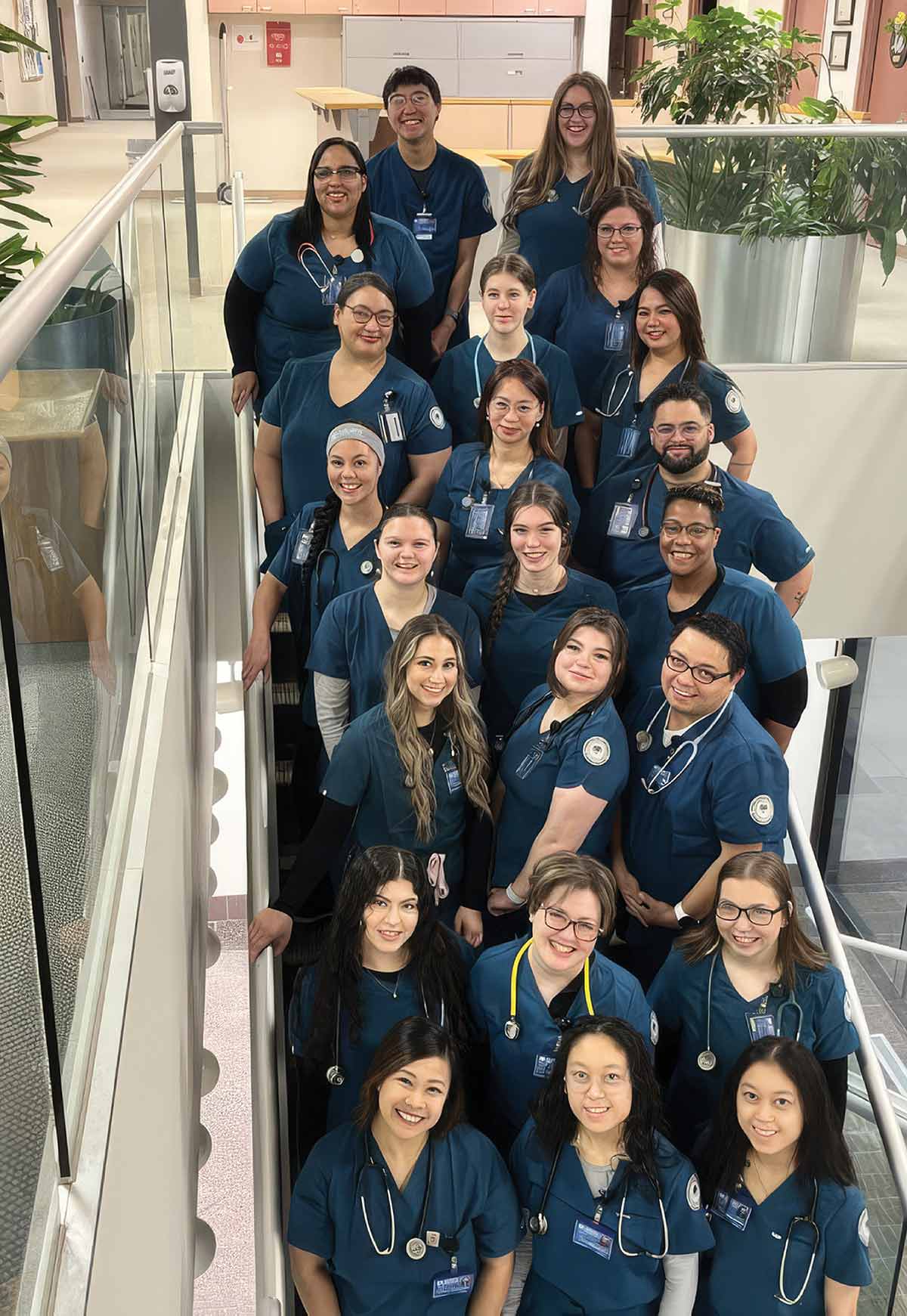 Group of nursing students wearing blue scrubs posing together on a staircase.