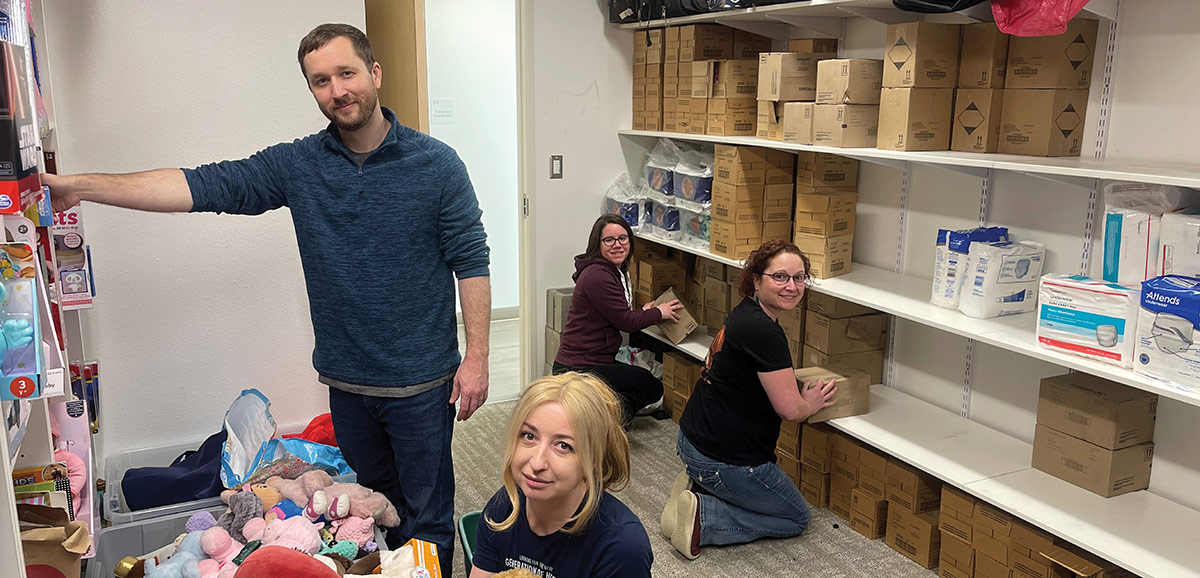 Volunteers organizing boxes, supplies, and plush toys in a storage room.