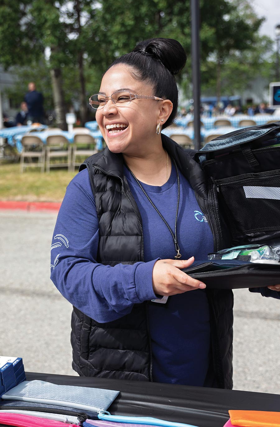 A smiling woman with glasses packing school supplies into a bag at an event.