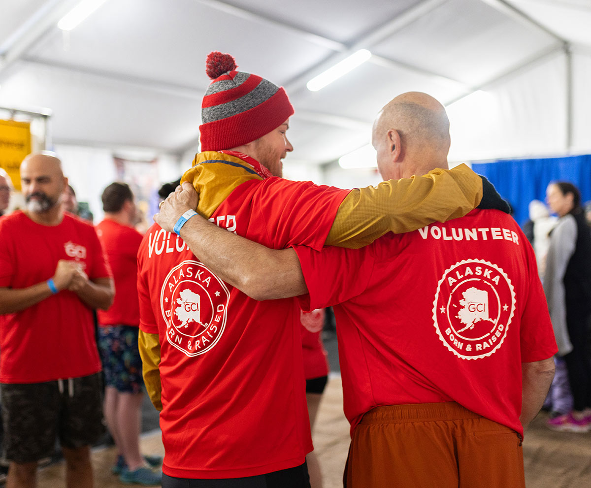 Two volunteers in red shirts putting their arms around each other at an event.