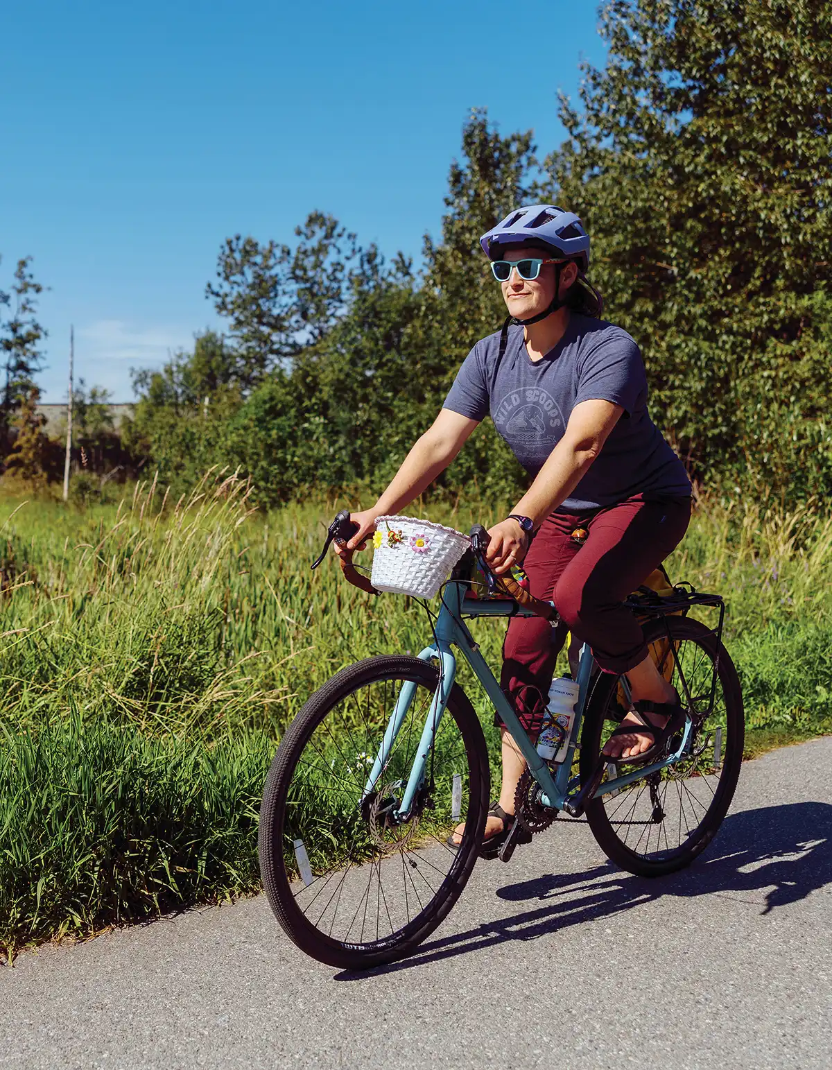 A cyclist wearing a helmet and sunglasses riding a bicycle along a paved path outdoors.