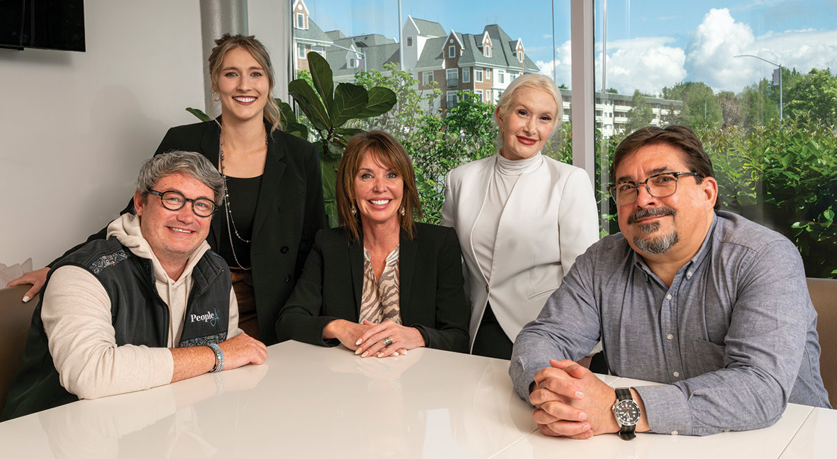 Five corporate colleagues smiling together around a conference table in a modern office space.
