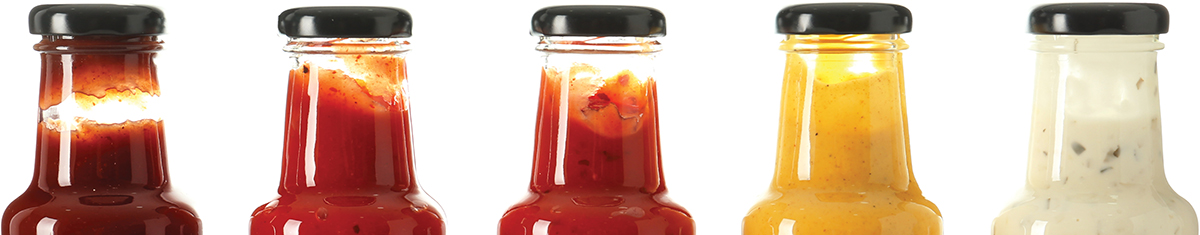 Row of five glass sauce bottles filled with various colorful sauces and condiments.